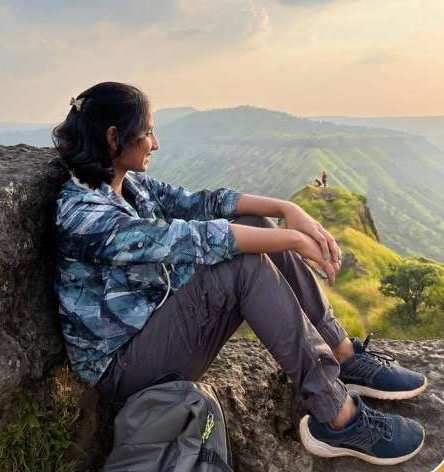 A trekker resting on a rock above a green valley